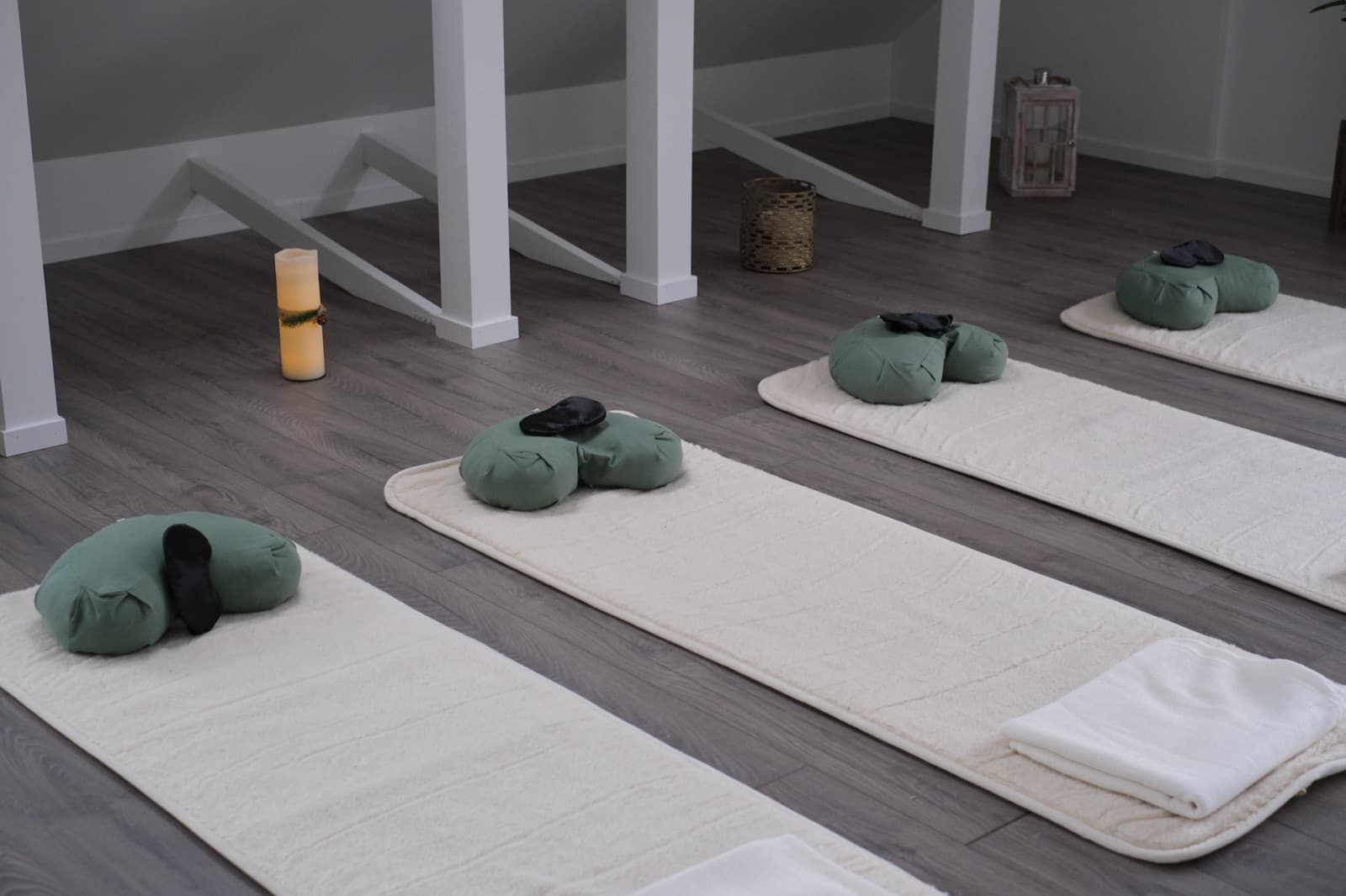 Mattor med gröna meditationskuddar och ögonmasker, ett tänt blockljus i bakgrunden